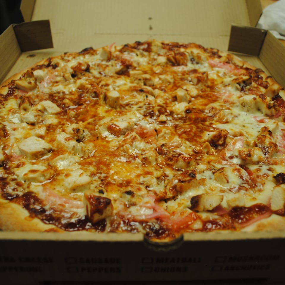 Blue Moon Pizzeria's BBQ chicken pizza, topped with melted cheese and red onions, in a delivery box.