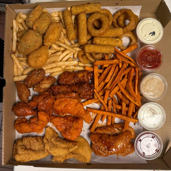 A pizza box filled with various fried foods including fries, onion rings, mozzarella sticks, and chicken.