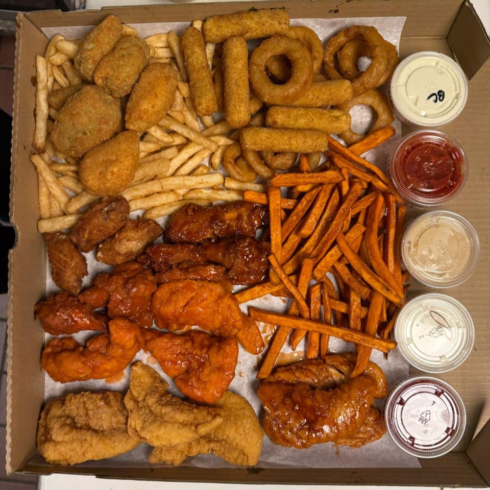 A pizza box filled with various fried foods including fries, onion rings, mozzarella sticks, and chicken.