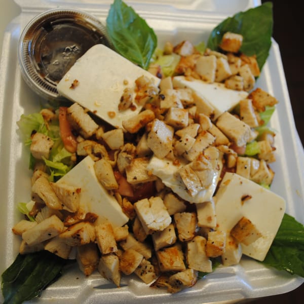 A takeout container filled with a salad of grilled chicken, feta cheese, lettuce, and dressing.