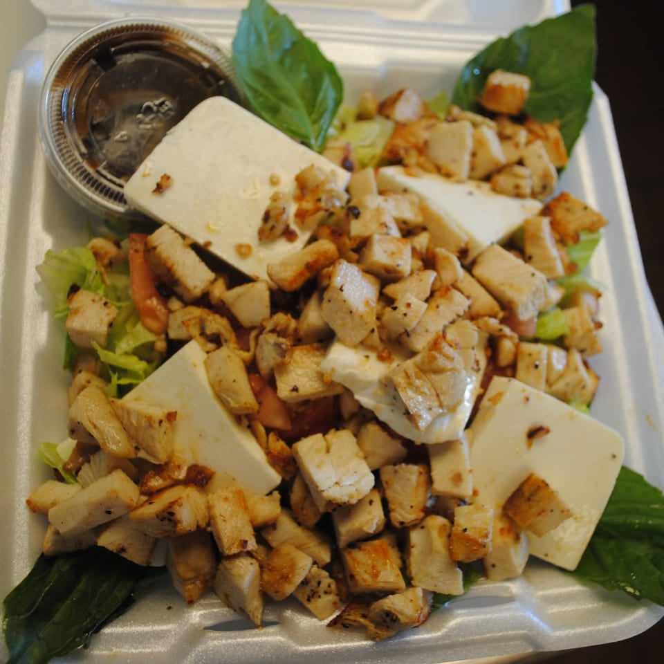 A takeout container filled with a salad of grilled chicken, feta cheese, lettuce, and dressing.