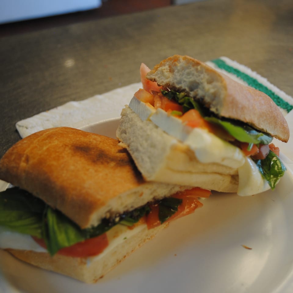 Two halves of a fresh caprese sandwich with mozzarella, tomato, and basil on a white plate.